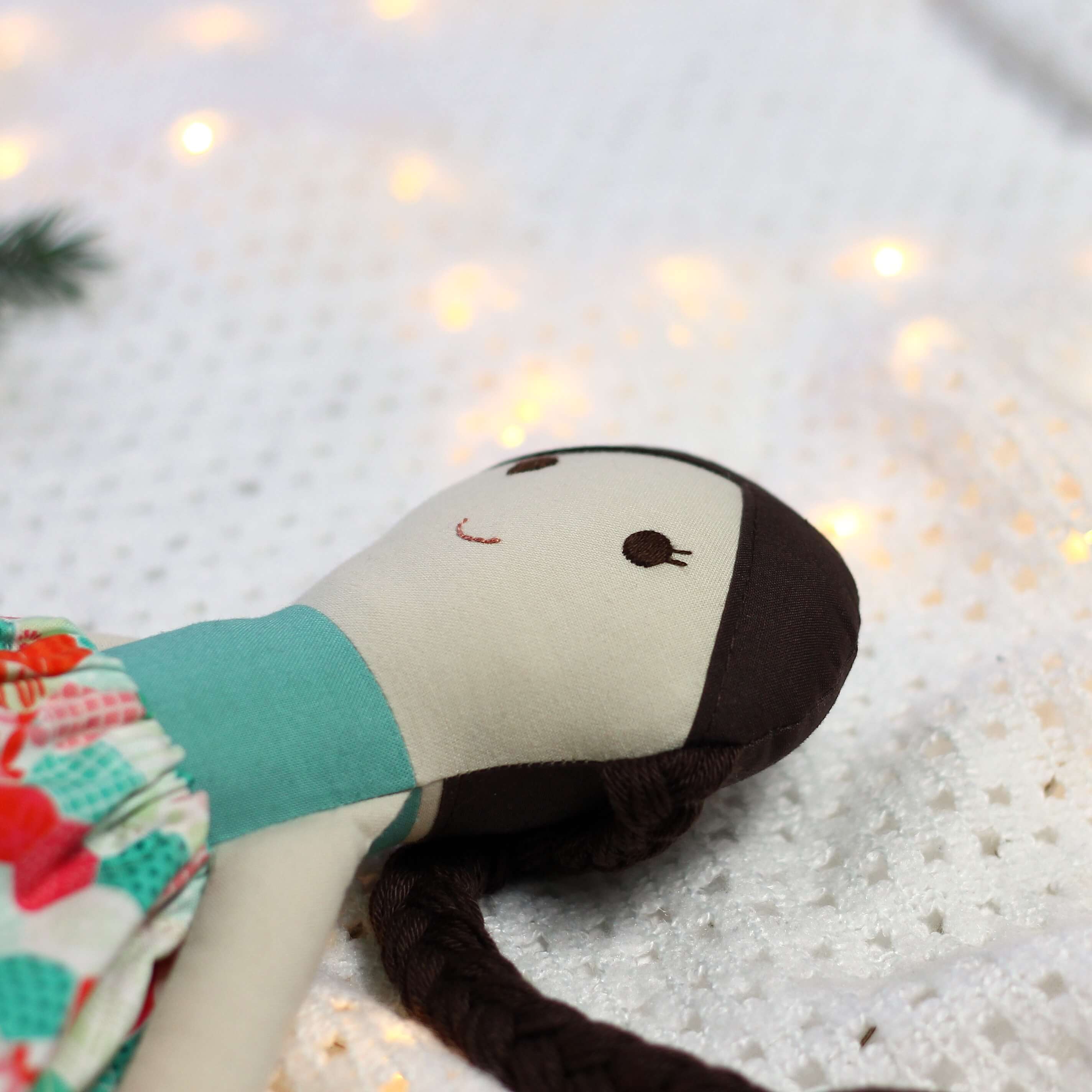 Zbliżenie na ręcznie szytą lalkę materiałową z naturalnych tkanin, z haftowaną twarzą i ciemnymi włosami zaplecionymi w warkocz